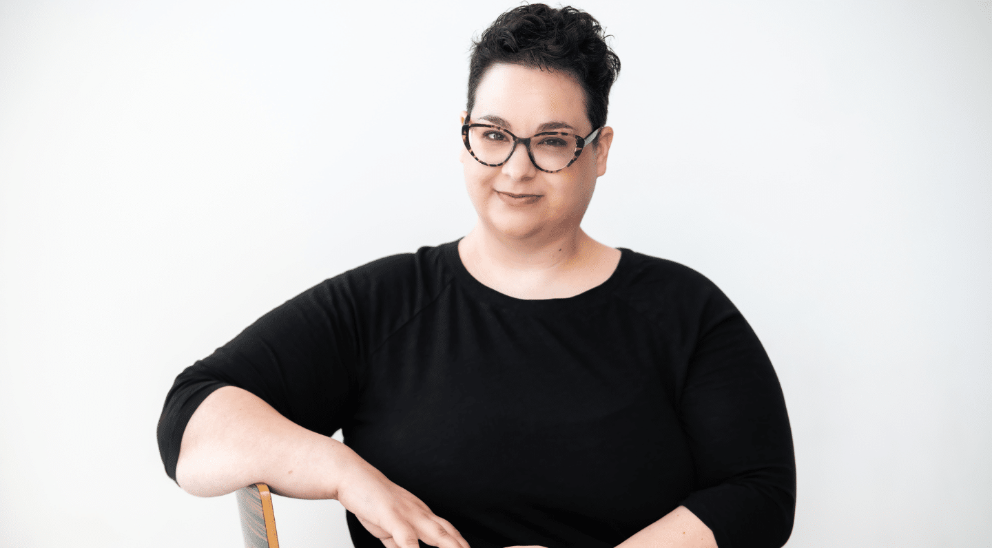 Ophira Calof seated with short dark hair, wearing glasses and a black three-quarter sleeve shirt.